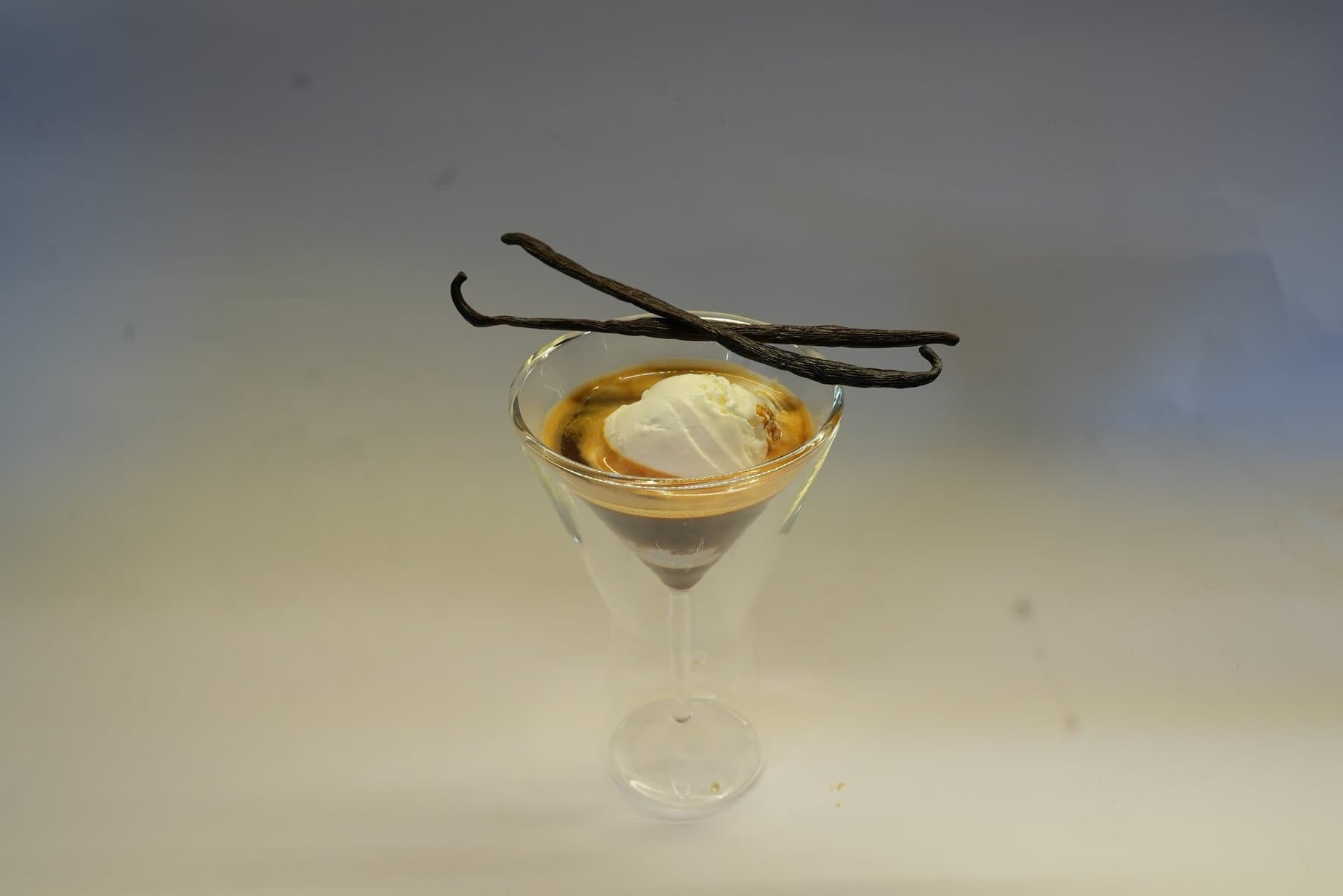 An affogato in a stemmed glass, topped with vanilla pods
