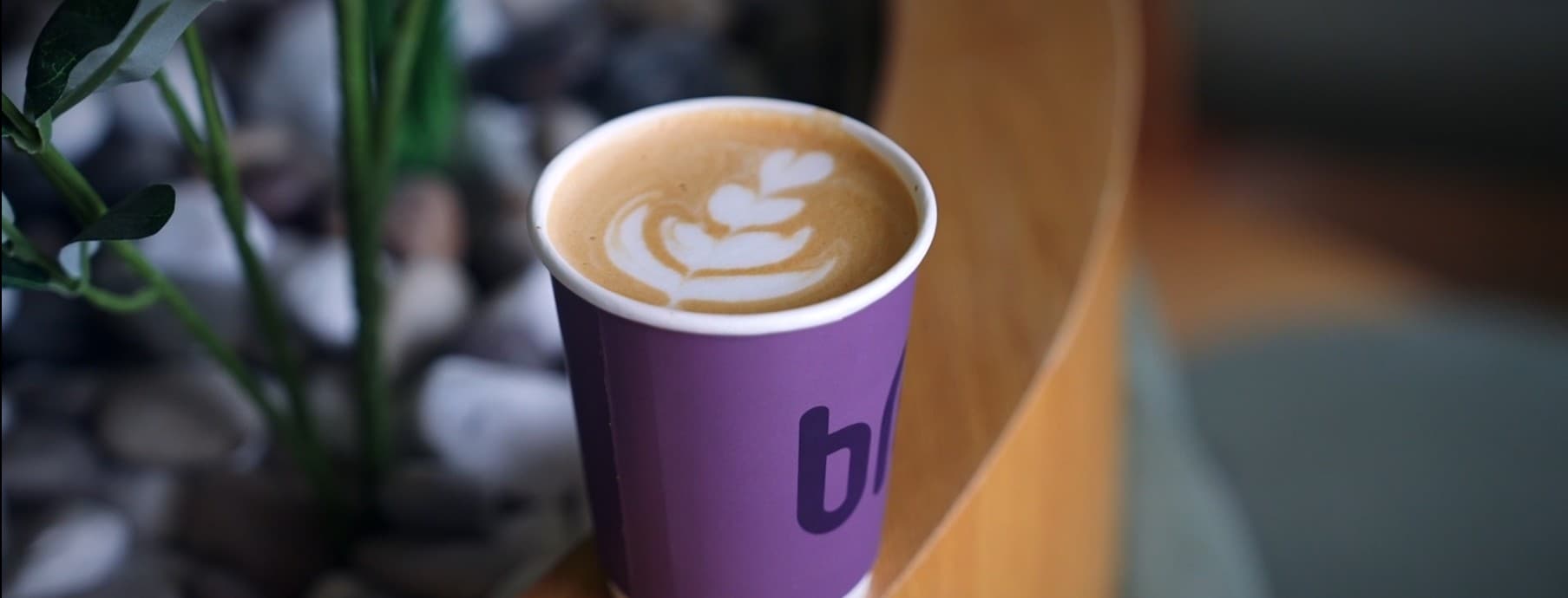A latte with heart-shaped latte art in a purple Brewed Rituals cup